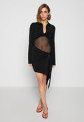 Schwarzes Kleid mit langen Ärmeln, einem durchsichtigen Mittelteil und einem Wickeldesign. Besitzt einen Kragen und eine Bindegurt-Akzent an der Taille. Rote Schuhe.