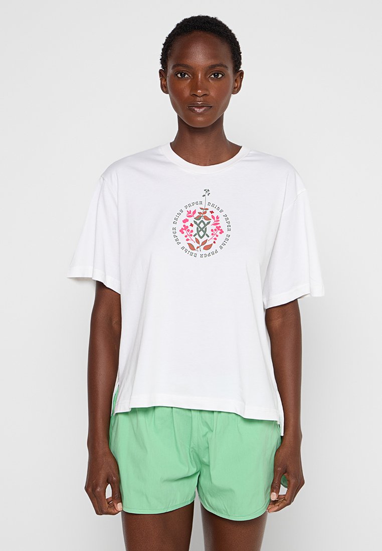 Weißes Baumwoll-T-Shirt mit Rundhalsausschnitt und kurzen Ärmeln, das ein florales Grafikdesign in Rosa und Grün zeigt. Getragen mit hellgrünen Shorts.