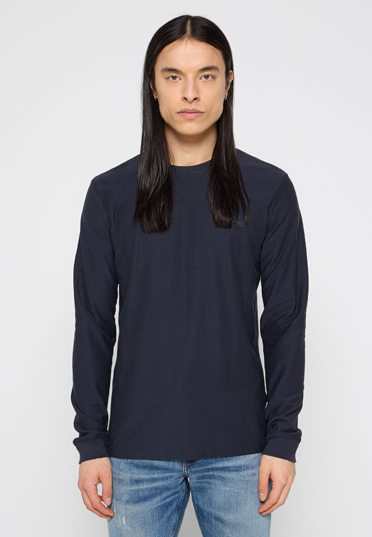 Marineblaues Langarmshirt aus strukturiertem Stoff, mit Rundhalsausschnitt und schmalen Ärmeln, kombiniert mit hellblauen, stark ausgewaschenen Jeans.