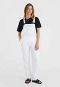 Weiße Denim-Overalls mit verstellbaren Trägern und einer Fronttasche, kombiniert mit einem schwarzen T-Shirt und schwarzen Badesandalen, in einem lässigen Schnitt.