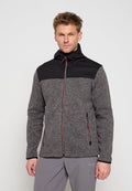 Mann trägt eine graue Fleecejacke mit schwarzen Schultern und roten Reißverschlussdetails, steht vor einem schlichten hellen Hintergrund.