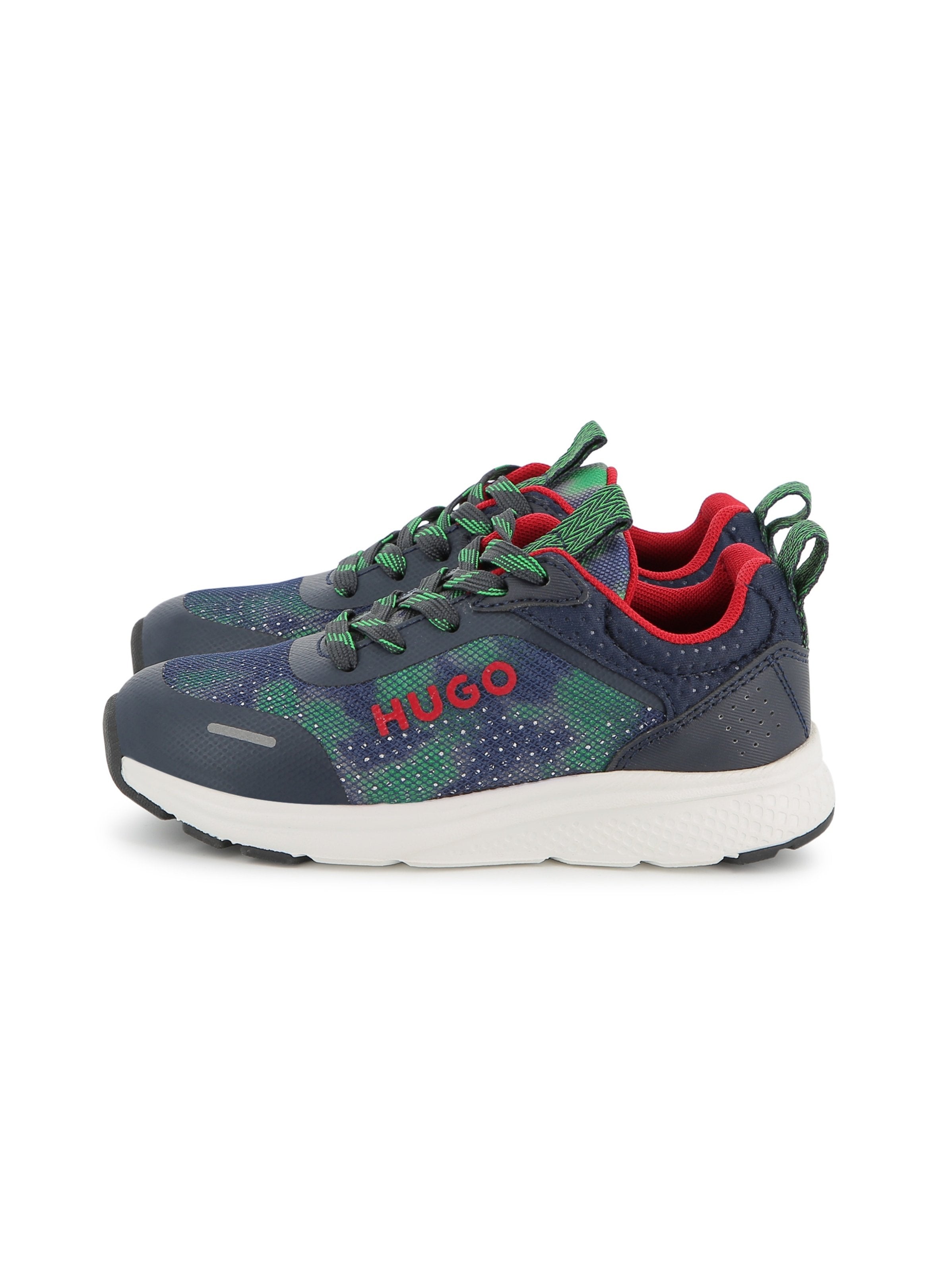 Sneaker haben ein navyfarbenes Obermaterial aus Synthetik mit grünem Camouflage-Muster, roten Akzenten und schwarzen Gummisohlen. Sie sind mit grünen Schnürsenkeln und einer geschlungenen Fersenschlaufe ausgestattet.
