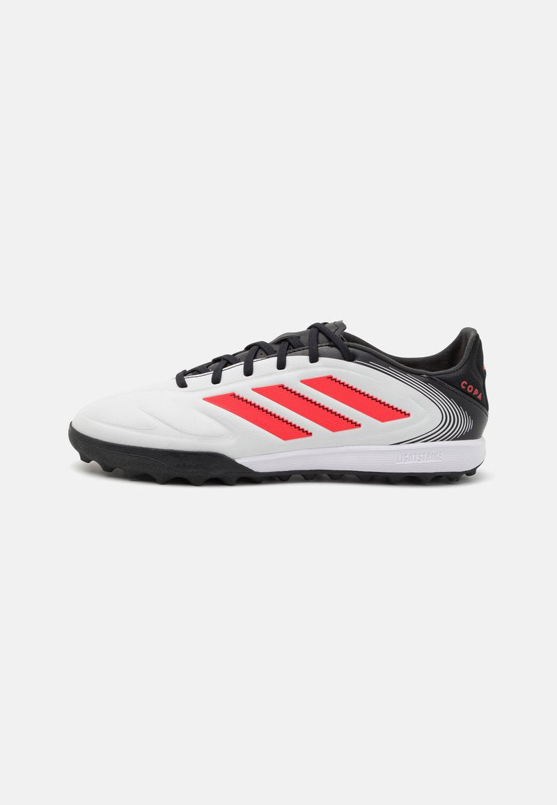 Weiße Fußballschuhe mit schwarzen Akzenten, die rote Streifen und eine strukturierte Oberfläche aufweisen. Für Kunstrasen konzipiert, mit einer Gummisohle für besseren Halt.