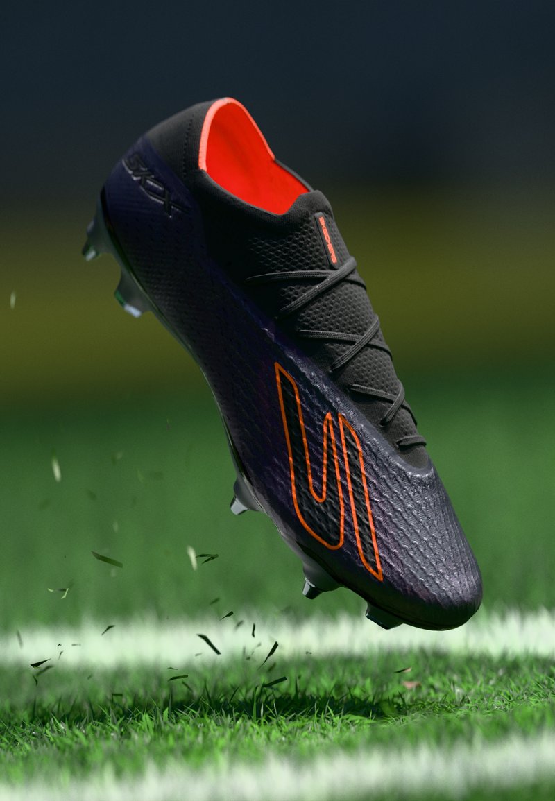 Schwarzer Fußballschuh mit orangefarbenen Akzenten, strukturiertem Obermaterial und schwarzen Schnürsenkeln, mit einem geschwungenen Design und Stollen, in der Luft über Gras eingefangen.