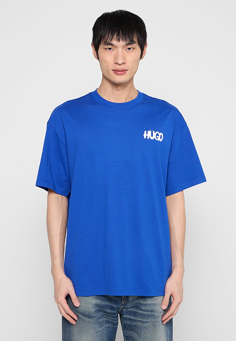 Blaues Baumwoll-T-Shirt mit kurzen Ärmeln, rundem Ausschnitt und weißem Logo auf der linken Brust. Lässige Passform und glatte Textur.