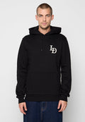 Mann in einem schwarzen Hoodie mit einer Vordertasche und "LD"-Logo auf der Brust, kombiniert mit blauen Jeans, steht vor einem einfarbigen Hintergrund.