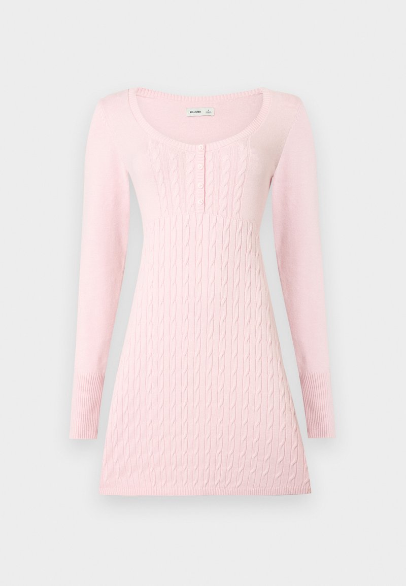 Hellrosa langärmliges Strickkleid mit Zopfmuster, rundem Ausschnitt und vier kleinen Knöpfen auf der Brust.