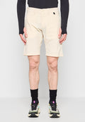 Mann trägt beige knielange Shorts, schwarzen Langarmoberteil, schwarze Socken und mehrfarbige Laufschuhe, steht vor einem schlichten Hintergrund.