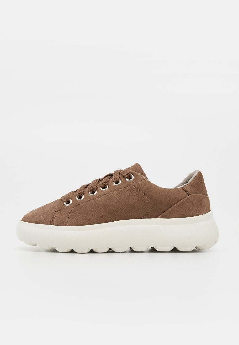 Brauner Wildleder-Sneaker mit dicker weißer profilierter Sohle, Metallösen und niedrigem gepolstertem Kragen auf weißem Hintergrund.