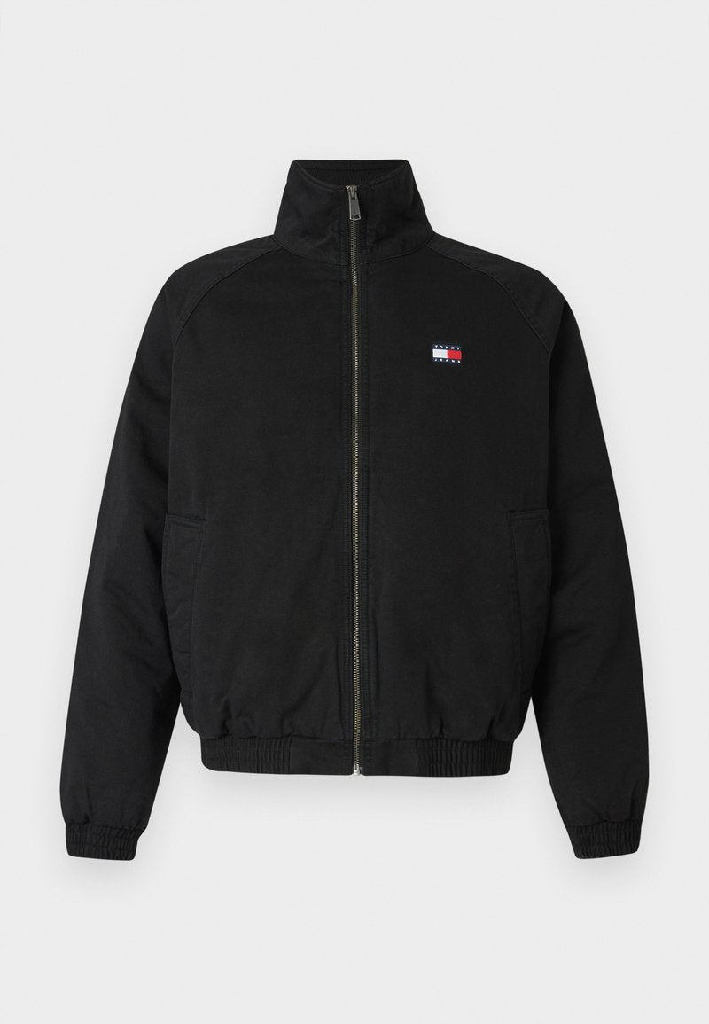 Schwarze Bomberjacke mit hohem Kragen, Frontreißverschluss, elastischen Bündchen und Saum, mit einem kleinen Logo in Rot, Weiß und Blau auf der Brust.
