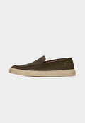 Olivgrüner Slip-On-Schmallederschuh mit einer cremefarbenen Gummisohle und einem kleinen mehrfarbigen Stoffetikett an der Seite.