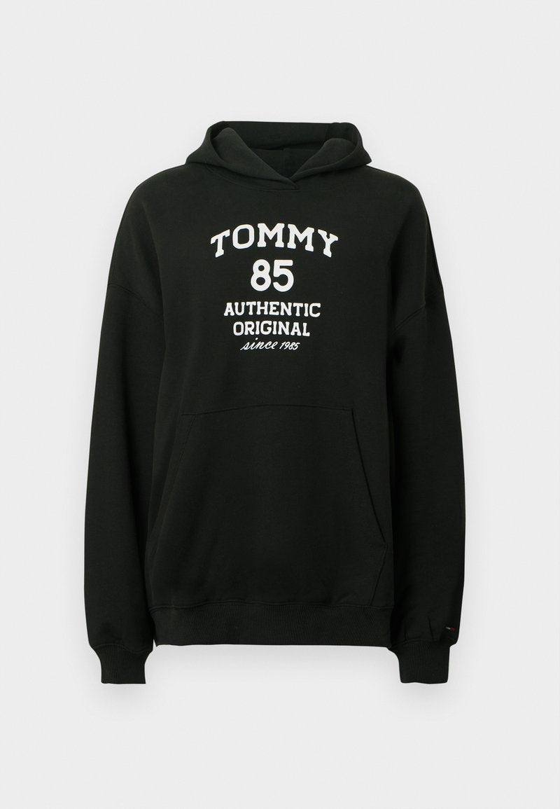 Schwarzer Hoodie aus weichem Stoff mit Kängurutasche. Auf der Vorderseite befindet sich weißer Text: "TOMMY 85 AUTHENTIC ORIGINAL seit 1985".