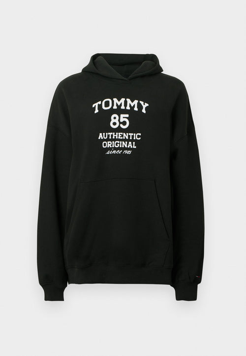 Schwarzer Hoodie aus weichem Stoff mit Kängurutasche. Auf der Vorderseite befindet sich weißer Text: "TOMMY 85 AUTHENTIC ORIGINAL seit 1985".
