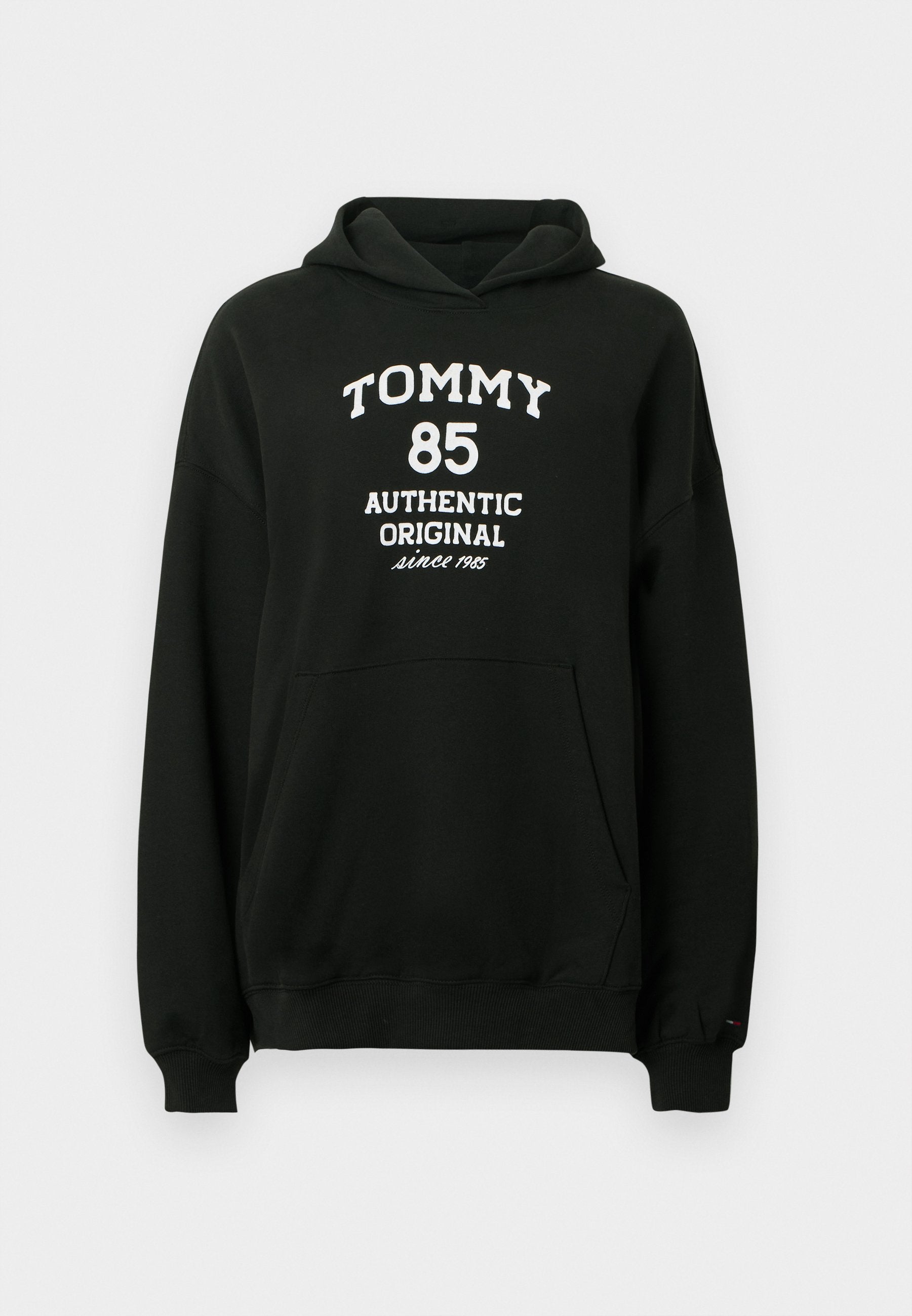 Schwarzer Hoodie aus weichem Stoff mit Kängurutasche. Auf der Vorderseite befindet sich weißer Text: "TOMMY 85 AUTHENTIC ORIGINAL seit 1985".