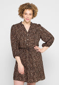Lächelnde Frau mit lockigem Haar, die ein knieumspielendes braun-schwarzes Leopardenmuster-Kleid mit Knöpfen und dreiviertellangen Ärmeln trägt.