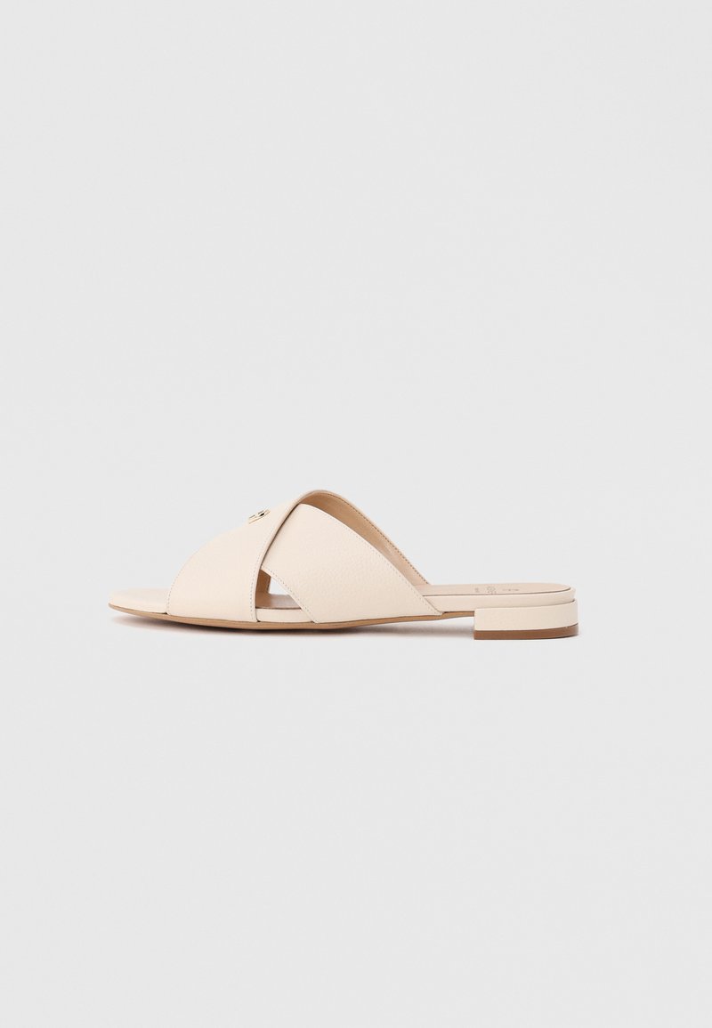 Beige Slide-Sandale mit gekreuzten Lederriemen und niedrigem Blockabsatz auf schlichtem hellgrauem Hintergrund.