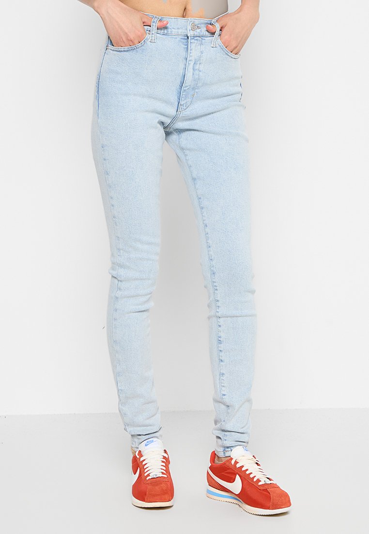 Helle blaue High-Waisted-Jeans mit schlanker Passform, klassischem Fünf-Taschen-Design und dezentem ausgewaschenem Look. Getragen mit roten Sneakers.