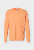 Langärmliges, pfirsichfarbenes Sportshirt mit Rundhalsausschnitt, hellrosa Adidas-Logo auf der Brust und drei Streifen an jedem Ärmel.