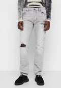 Graue Jeans aus Denim mit einer lockeren Passform, die ausgefranste Stellen, fransige Säume und einen klassischen Fünf-Taschen-Stil aufweisen, kombiniert mit schwarzen Schuhen.