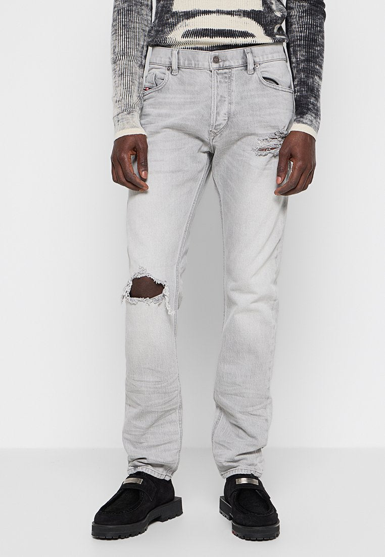 Graue Jeans aus Denim mit einer lockeren Passform, die ausgefranste Stellen, fransige Säume und einen klassischen Fünf-Taschen-Stil aufweisen, kombiniert mit schwarzen Schuhen.