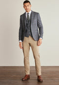 Grau karierter Blazer mit Reverskragen über einer passenden Weste, kombiniert mit beigen Hosen und braunen Lederstiefeln. Glatte Textur und taillierte Passform.
