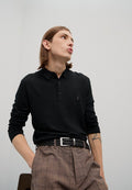Schwarzes Langarm-Polohemd mit zwei Knöpfen, kombiniert mit braunen karrierten Hosen und einem geflochtenen schwarzen Gürtel. Leichte Textur, lässige Passform.