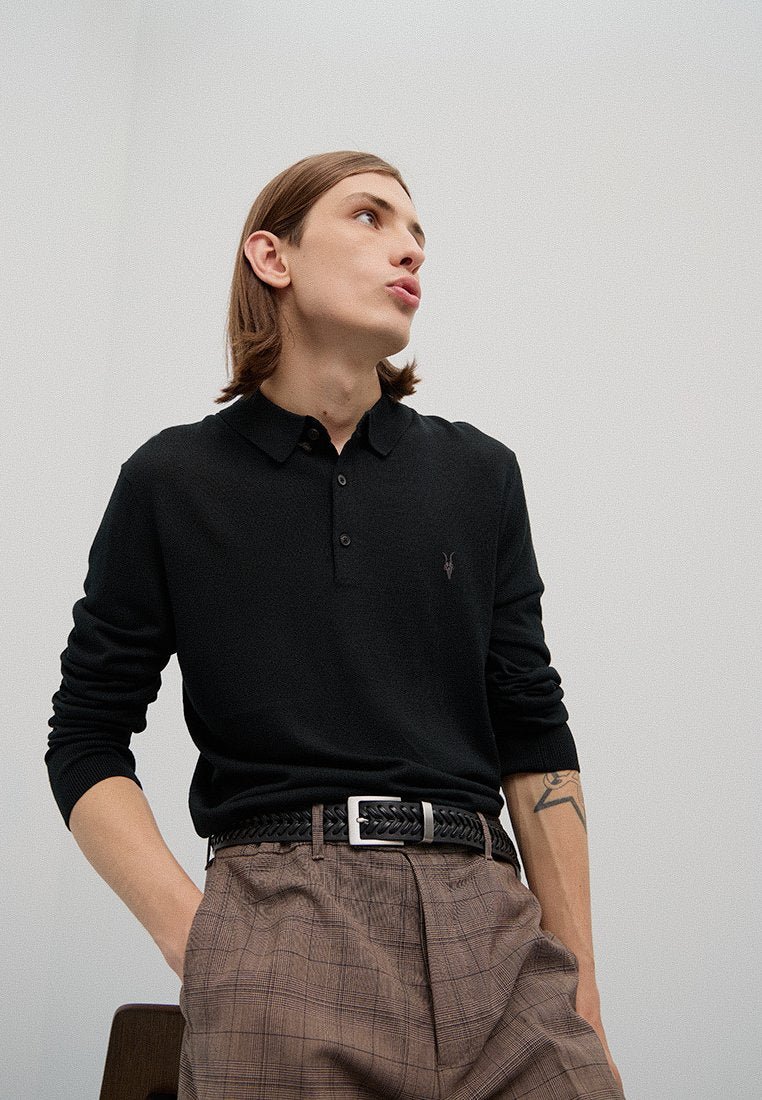 Schwarzes Langarm-Polohemd mit zwei Knöpfen, kombiniert mit braunen karrierten Hosen und einem geflochtenen schwarzen Gürtel. Leichte Textur, lässige Passform.