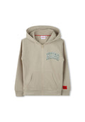 Beige Zip-Hoodie aus weichem Material. Mit großem grünen "HUGO"-Logo, zwei Fronttaschen und einem roten Etikett in der unteren rechten Ecke.