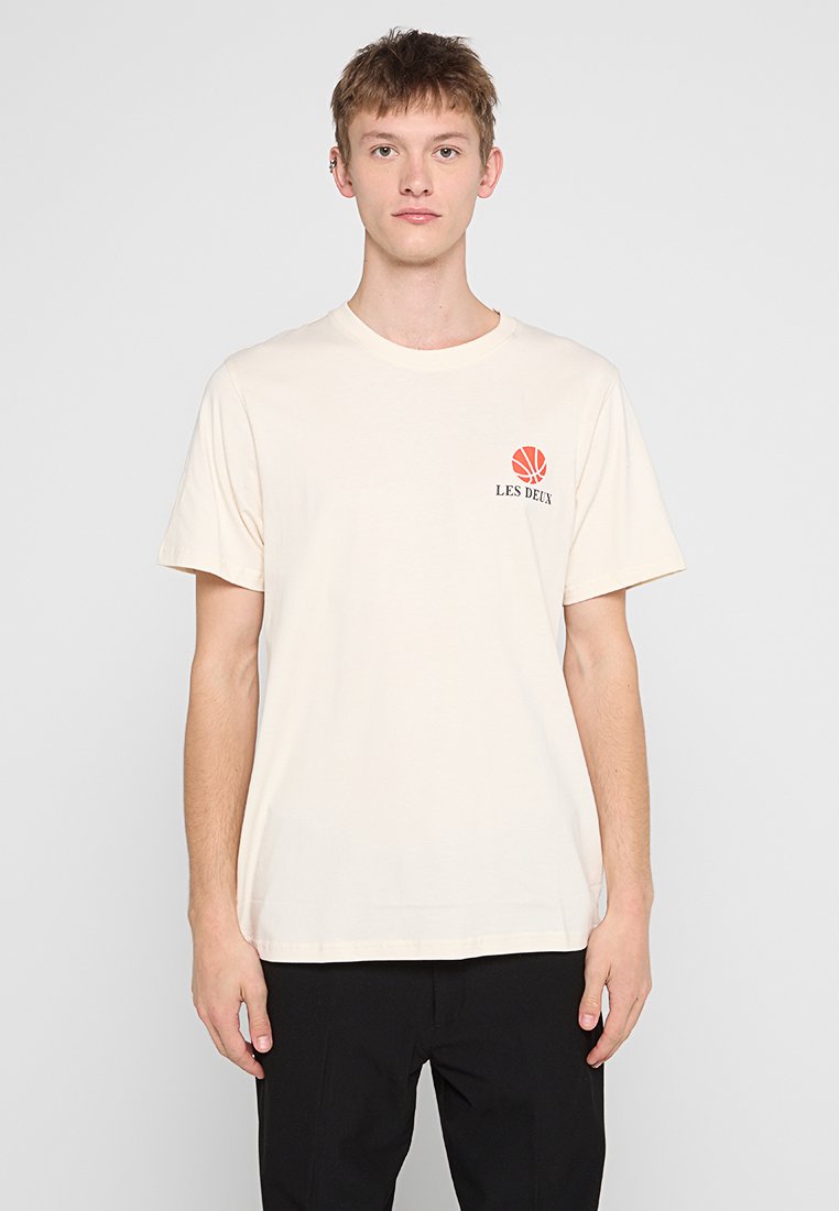 Cremfarbener Baumwoll-T-Shirt mit kurzen Ärmeln, Rundhalsausschnitt und einem kleinen roten Basketball-Graphic über dem Text "LES DEUX" auf der linken Brust.