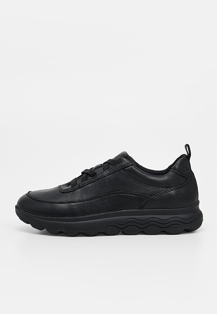 Schwarzer Ledersneaker mit Schnürdesign, gepolstertem Kragen und dicker, strukturierter Sohle, von der Seite auf weißem Hintergrund gezeigt.