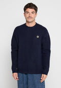 Dunkelblauer Strickpullover mit rundem Halsausschnitt, gerippten Ärmeln und einem kleinen gestickten Logo auf der Brust. Weiche Textur, entspannte Passform.