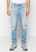Hellblaue Denim-Jeans mit lockerer Passform, die an den Knien aufgerissene Stellen und dezente Verwaschungen aufweisen. Kombiniert mit grauen Sportschuhen.