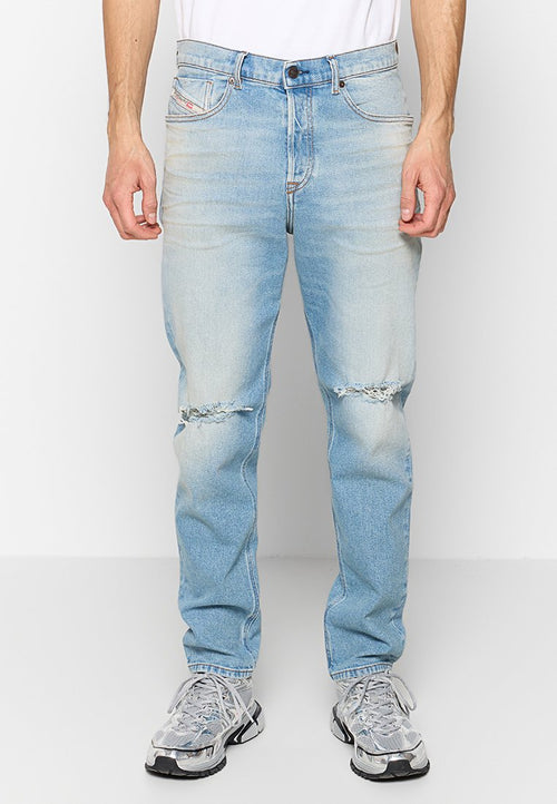 Hellblaue Denim-Jeans mit lockerer Passform, die an den Knien aufgerissene Stellen und dezente Verwaschungen aufweisen. Kombiniert mit grauen Sportschuhen.