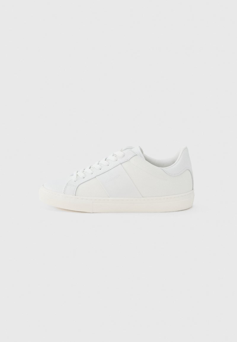 Weißer Sneaker mit niedrigem Schaft, Schnürung vorne und elfenbeinfarbener Gummisohle, von der Innenseite auf hellem grauem Hintergrund gezeigt.
