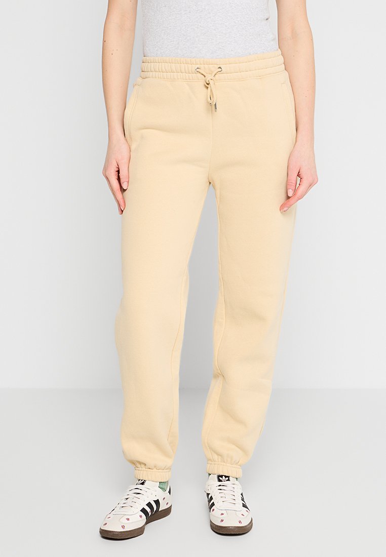 Beige Sweatpants aus einem Baumwollmix mit elastischem Bund, verstellbarem Kordelzug, schmal zulaufenden Beinen und Seitentaschen. Kombiniert mit gemusterten Turnschuhen.