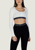 Weißes, geripptes Crop-Top mit langen Ärmeln und Knopfdetails sowie einem schwarzen elastischen Bund mit dem "TOMMY JEANS"-Logo; kombiniert mit hoch taillierten schwarzen Leggings.