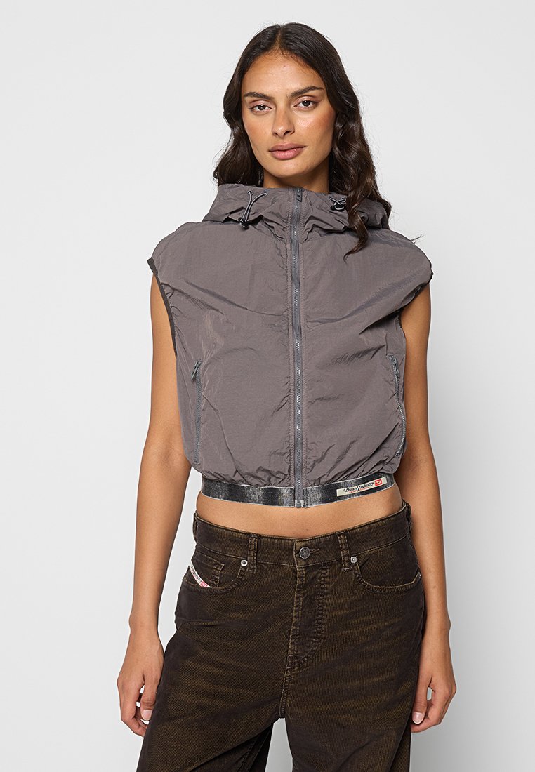 Gekürzte ärmellose Jacke aus grauem Nylon mit durchgehendem Reißverschluss, Kordelzugkapuze und reflektierendem Taillenbund. Kombiniert mit dunkel gefärbten, strukturierten Hosen.