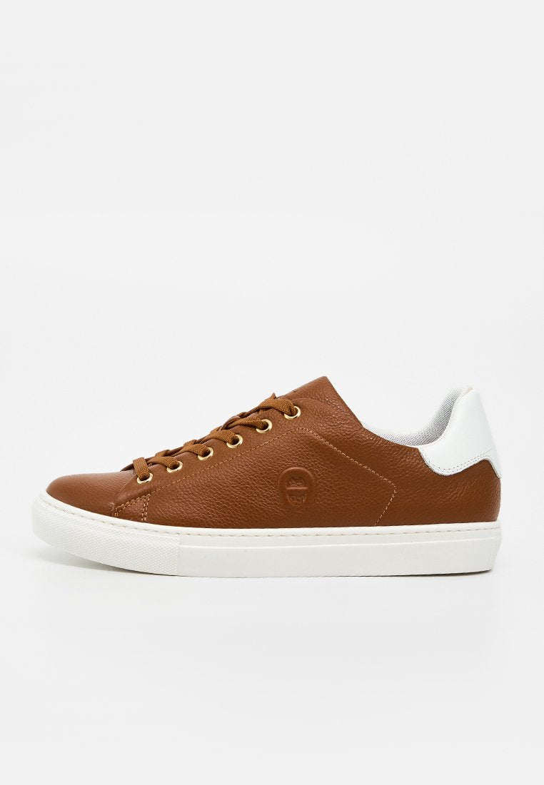 Brauner Leder-Low-Top-Sneaker mit weißem Fersenakzent, weißer Gummisohle, braunen Schnürsenkeln und goldenen Ösen, seitlich auf weißem Hintergrund gesehen.