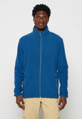 Mann in einer blauen Fleecejacke mit Reißverschluss und beigen Cargo-Hosen, der vor einem schlichten weißen Hintergrund steht.