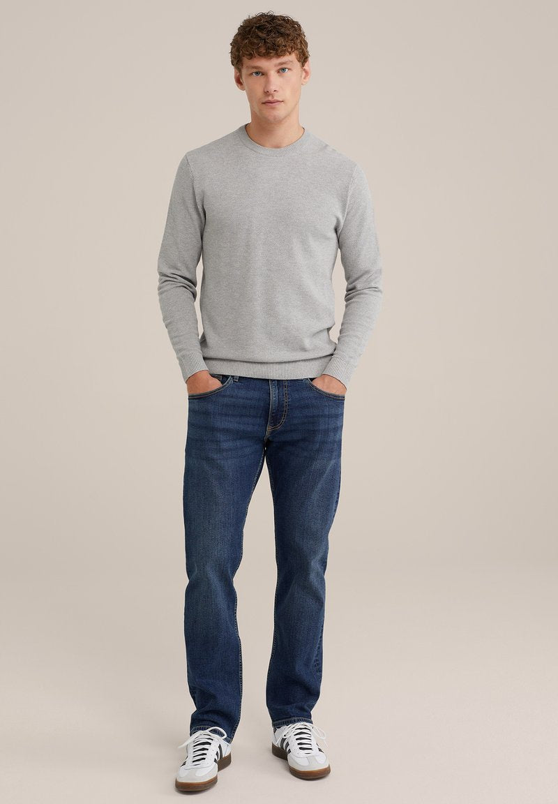 Grau gestrickter Pullover mit Rundhalsausschnitt und geripptem Saum, kombiniert mit dunkelblauen Denim-Jeans. Weiße Sneakers mit braunen Akzenten runden das Outfit ab.