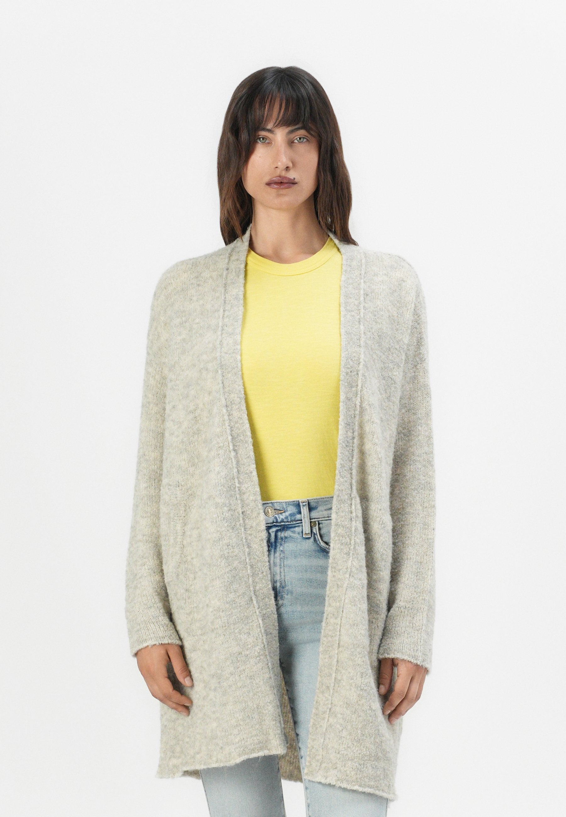 Helles graues, oversized Cardigan aus weichem Material, mit offenem Vorderteil, langen Ärmeln und strukturierter Oberfläche, kombiniert mit einem gelben Hemd.