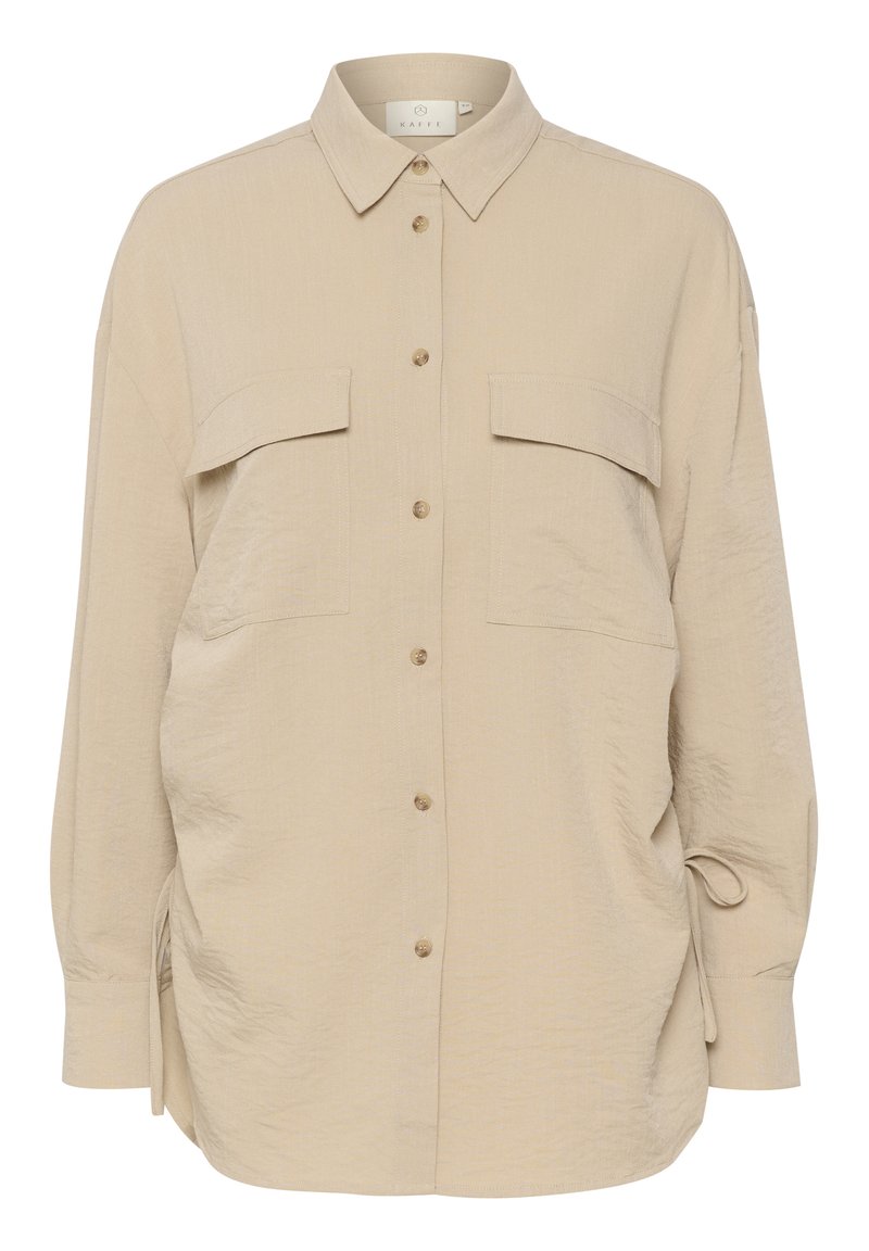 Beige Hemd mit Knopfverschluss aus weichem, strukturiertem Stoff, zwei Brusttaschen und seitlichen Bindebändern. Verfügt über einen klassischen Kragen und einen abgerundeten Saum.