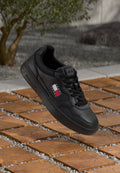 Schwarzer Leder-Sneaker mit perforierter Zehenpartie, flachen Schnürsenkeln und gesticktem Logo. Verfügt über eine Low-Top-Silhouette und eine Gummisohle, präsentiert auf strukturierten Fliesen.