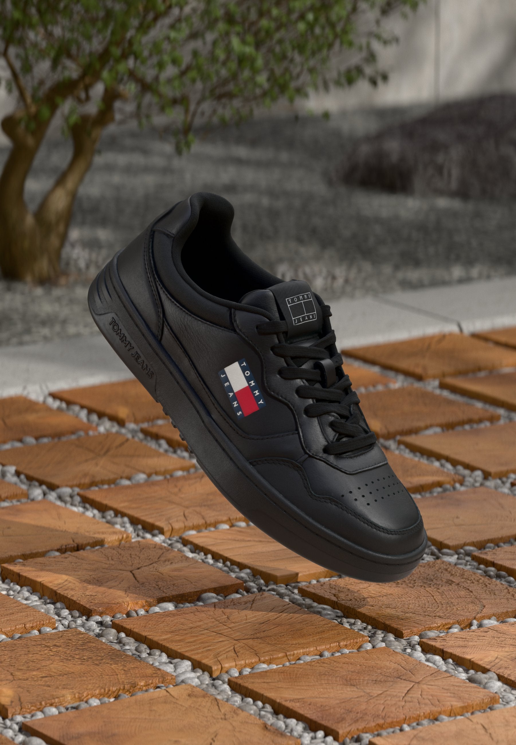 Schwarzer Leder-Sneaker mit perforierter Zehenpartie, flachen Schnürsenkeln und gesticktem Logo. Verfügt über eine Low-Top-Silhouette und eine Gummisohle, präsentiert auf strukturierten Fliesen.