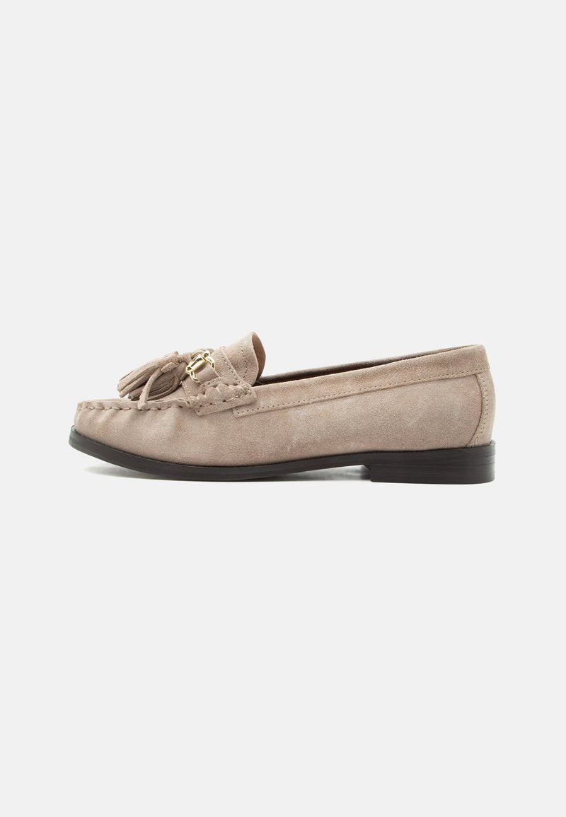 Beiger Wildleder-Slipper mit dekorativen Quasten und goldfarbenem Schnallenverschluss, flache schwarze Sohle und angenähte Details entlang der oberen Kante.