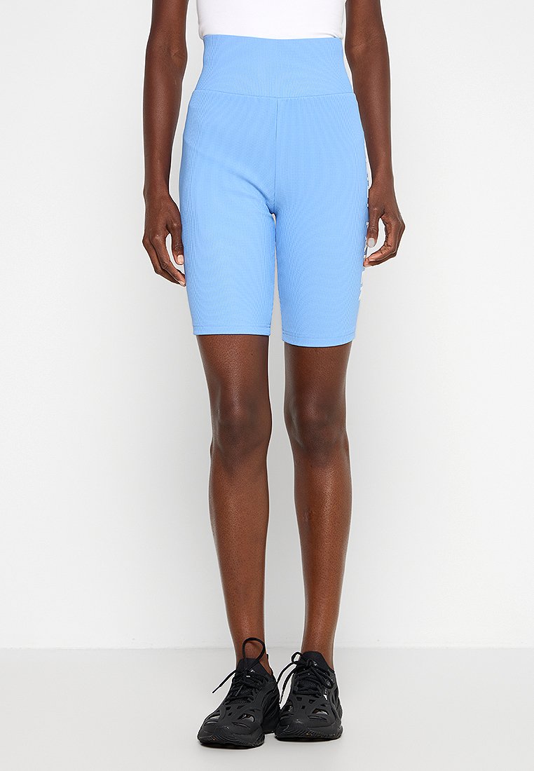 Hellblaue Radshorts mit hohem Bund, aus geripptem Stoff gefertigt. Sie verfügen über eine glatte Textur und ein körperbetontes Design, kombiniert mit schwarzen Turnschuhen.