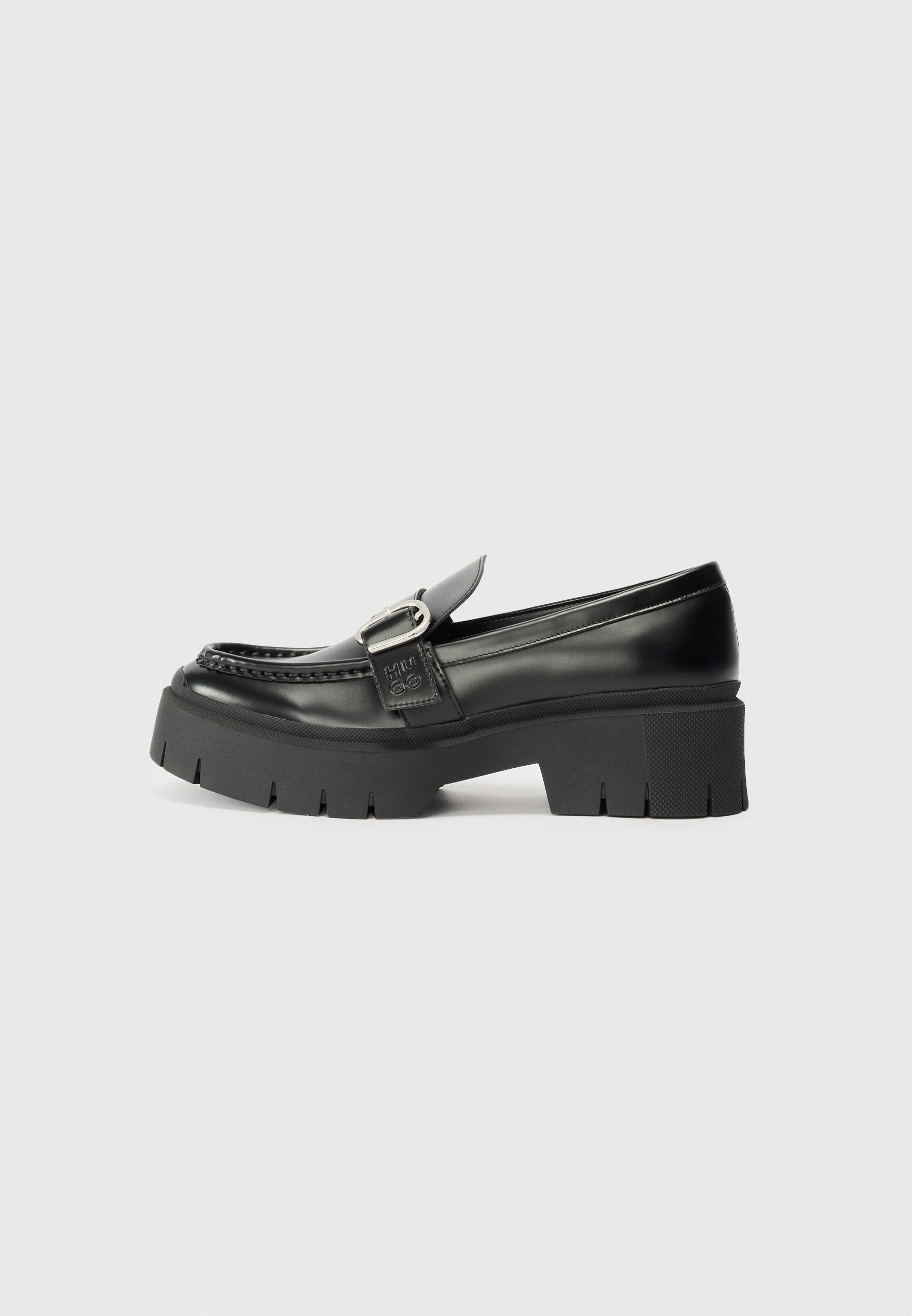Schwarze Leder-Lederschuhe mit dicker Gummisohle. Merkmale einen Schnallenakzent und gestickte Details entlang des Obermaterials. Flacher Absatz.