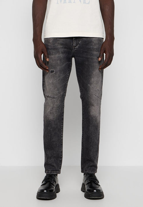 Schwarze Jeans aus Denim mit einem ausgebleichten und lädierten Textur, mit Rissen an den Knien und einem schmalen Schnitt. Getragen mit schwarzen Schnürschuhen.