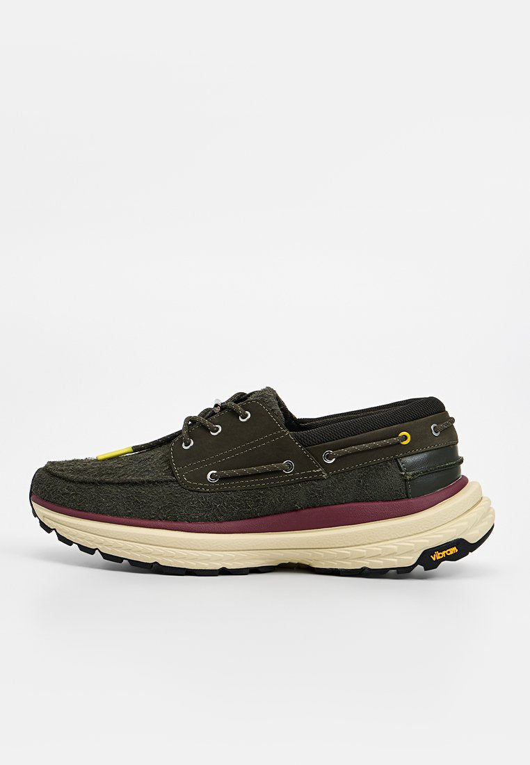 Grüne Stoffschuhe mit strukturierter Oberseite, einer kastanienbraunen Zwischensohle, schwarzen Akzenten und gelben Beschlägen. Gefertigt mit einer Vibram-Außensohle.