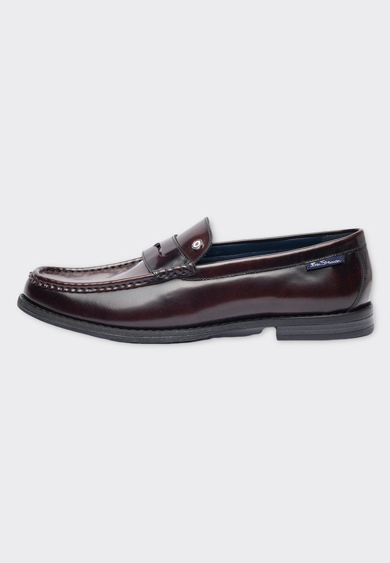 Braune Lederloafers mit glänzendem Finish, dekorativer Naht und einem kleinen Akzent am Riemen. Flache Gummisohle für Komfort.